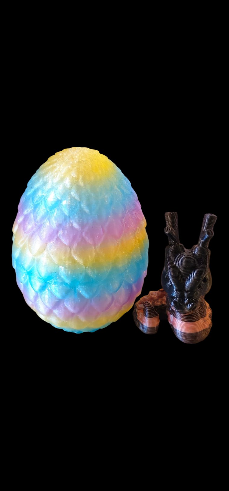 Rainbow pastel scaled dragon egg next to a small black and copper mini dragon