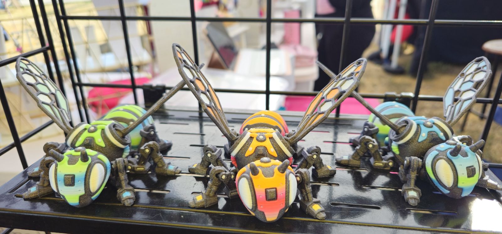 Three articulated mechanical bees in green, orange and blue with honeycomb wings