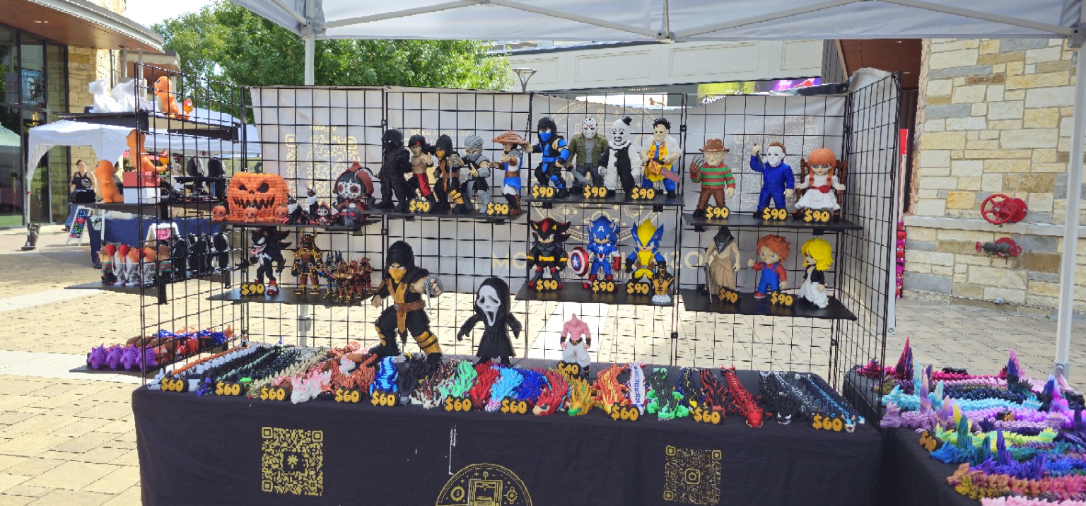 Full outdoor Kosmo Lux 3D booth with large printed characters, colorful dragons, and the market street behind